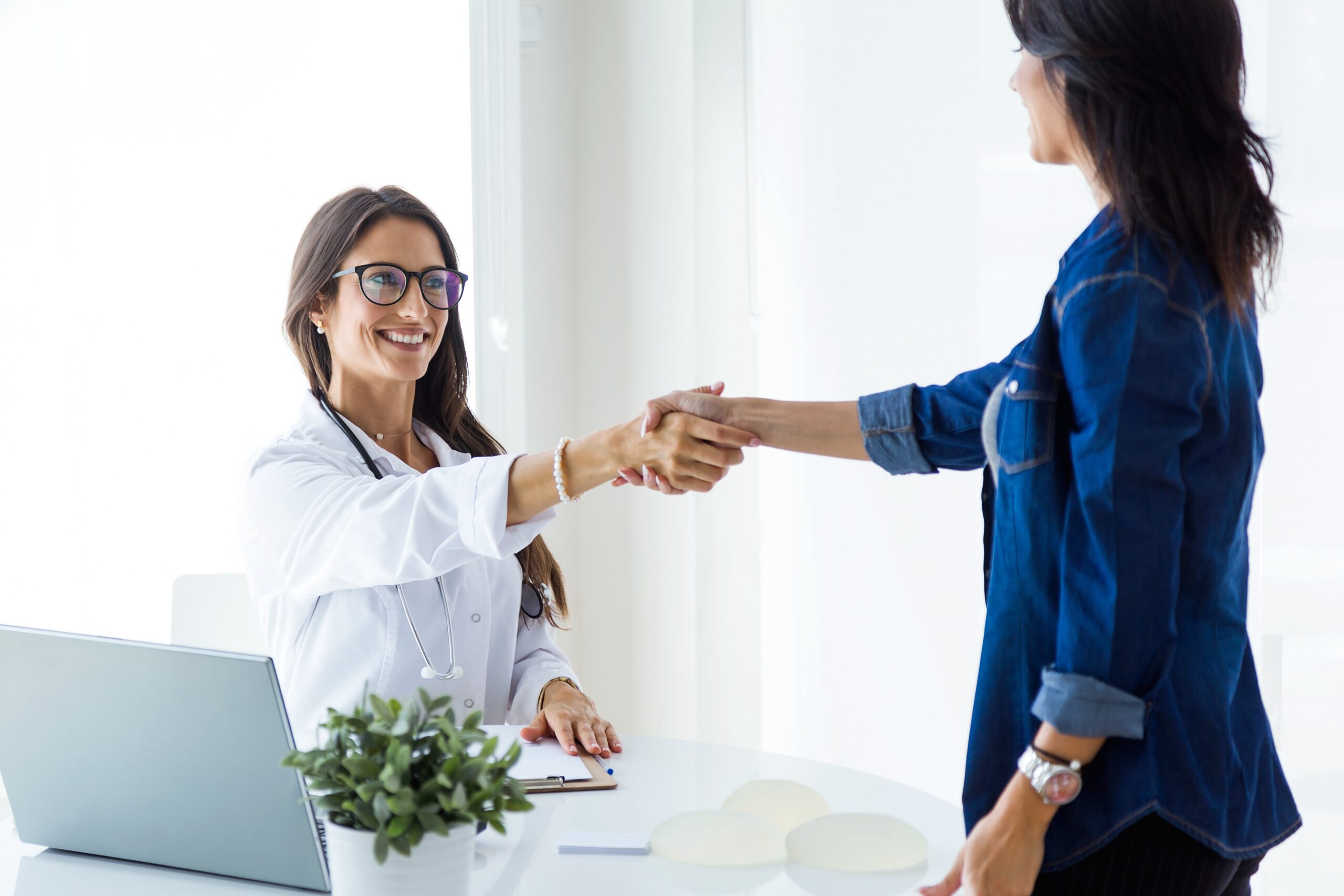 Female doctor and her patient shaking hands in the consultation.